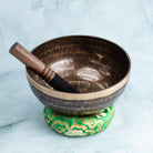 Singing bowl with wooden striker on a green cushion